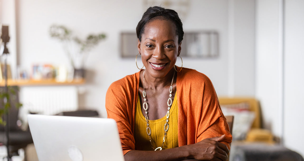 African American woman sitting in front of open laptop signaling signing up for an email list