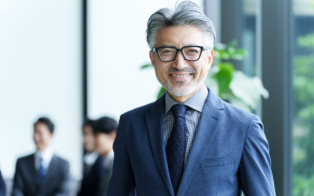 Older Asian man in navy linen suit smiling at camera